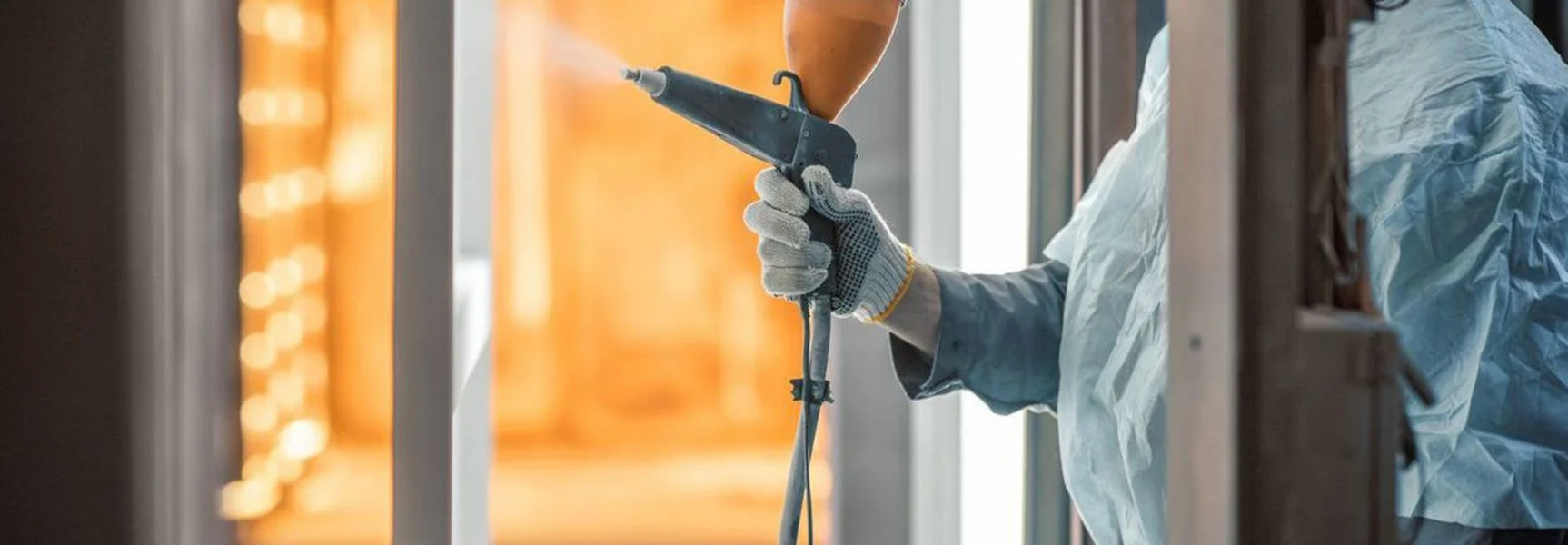 A man spraying powder coating on a hung metal substrate