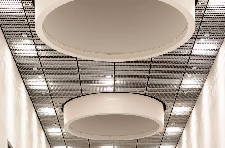 Long haalway with white walls and a black staircase at the end, decorated with 3 large, round, light screens at the ceiling