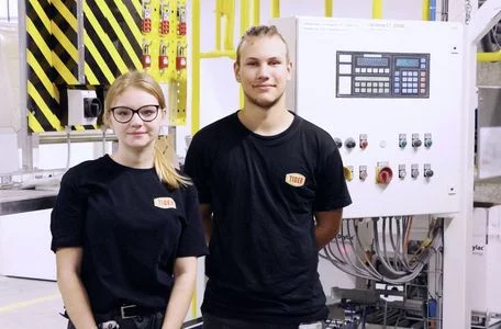 zwei TIGER-Auszubildende stehen vor einer TIGER-Produktionsmaschine